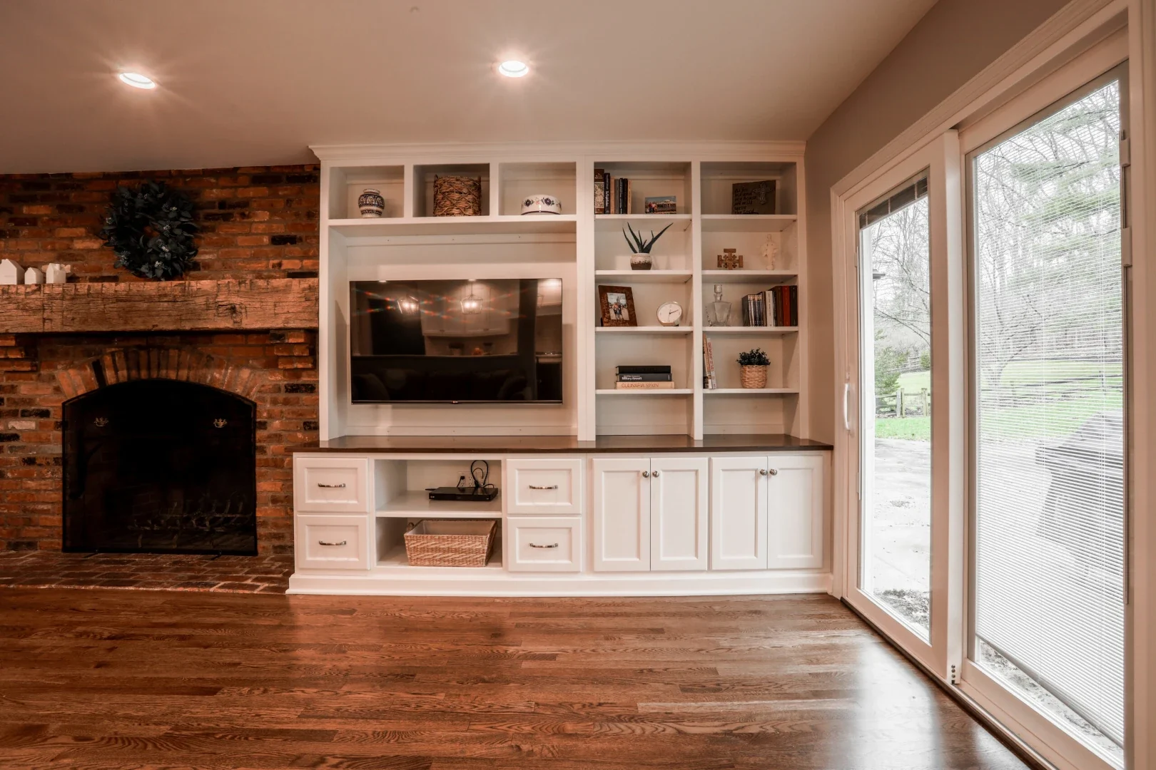 Built-in white media wall with open shelving beside an exposed brick fireplace